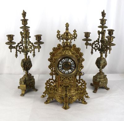 trois bougeoirs en laiton et une horloge posés sur une table