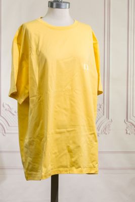 Le t-shirt jaune est posé sur un mannequin devant un mur.