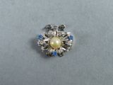a close up of a brooch with a pearl and blue stones