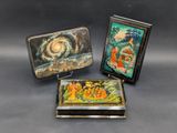 trois petites boîtes en métal ornées de peintures, posées sur une table