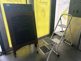 un petit tabouret posé à côté d'un tableau noir posé à même le sol