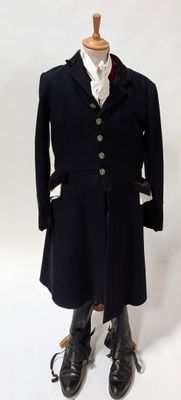 un manteau noir sur un mannequin, avec une chemise blanche et des bottes noires