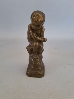 une petite statue en bronze représentant un garçon assis sur une souche d'arbre