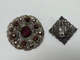 two silver and red brooches on a white surface
