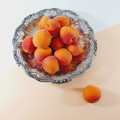 a bowl of apricots sitting on a table next to two oranges