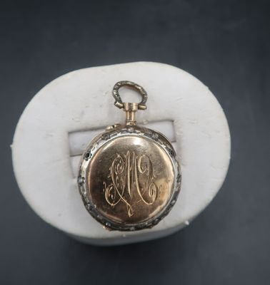 a close up of a gold pocket watch with a monogram on it