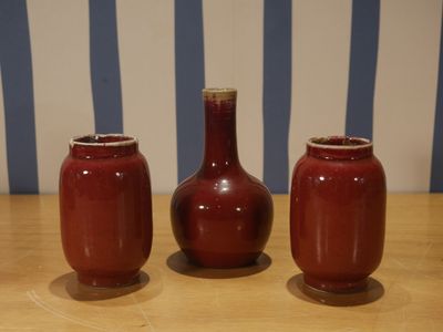 trois vases rouges posés sur une table en bois, près d'un mur rayé