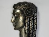 une sculpture métallique représentant la tête d'une femme sur fond blanc
