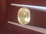 un diamant jaune de forme ovale est maintenu par une paire de pinces