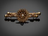 un gros plan sur une broche en forme de fleur, en or et perles