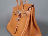 tan leather handbag with two handles on a grey background