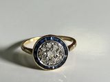 a close up of a gold ring with a diamond and blue sapphire