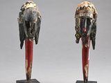 une paire de masques en bois sculptés posés sur des socles, sur une surface grise