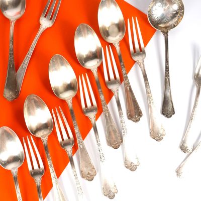 de nombreuses cuillères et fourchettes en argent sur un fond orange et blanc