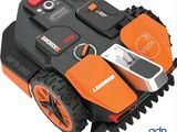 an orange and black robotic lawn mower sitting on top of a white surface