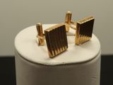 a close up of a pair of gold cufflinks on a white stand