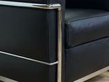 black leather lounge chair with chrome legs and arm rests against a white wall