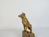 statue en laiton représentant un chien assis sur un rocher, sur fond blanc