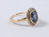 a close up of a gold ring with a blue stone surrounded by diamonds
