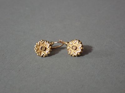 un gros plan sur une paire de boucles d'oreilles en or posées sur une surface grise
