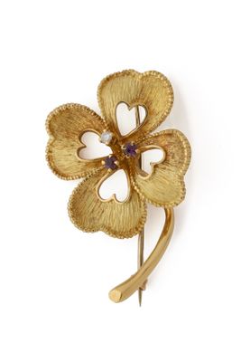 une image représentant une broche en forme de fleur en or, ornée d'une pierre violette en son centre