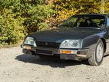 a black car parked on a gravel road in front of some trees