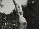 black and white photograph of a woman in a bathing suit reaching up to catch a frisbee