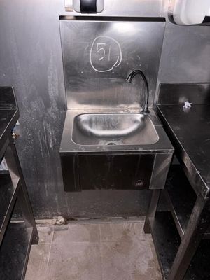 un lavabo en métal dans des toilettes publiques, avec des plans de travail noirs