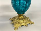 a blue vase sitting on a gold stand on a white surface