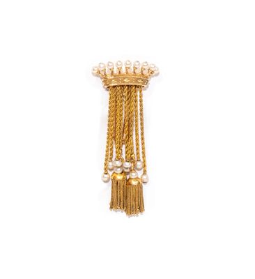 un gros plan sur une broche en or ornée de perles et de pompons