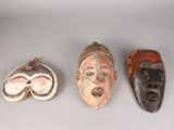 Trois masques en bois sont posés les uns à côté des autres sur une table