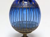 a blue glass egg on a gold stand on a white surface