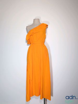 une robe orange posée sur un mannequin, devant un mur blanc