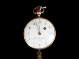 a gold clock hanging from a chain on a black background