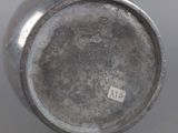an old silver vase sitting on top of a table next to a white wall