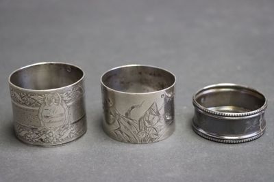 trois ronds de serviette en argent ornés de motifs, posés sur une table