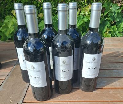 six bottles of wine sitting on a wooden table in front of a bush