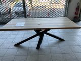 a wooden table with a metal cross base in the middle of a room