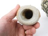 a hand holding a small vase with a hole in it