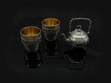 trois tasses en argent et une théière posées sur un support noir