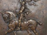 bronze plaque depicting a man on a horse holding a flag