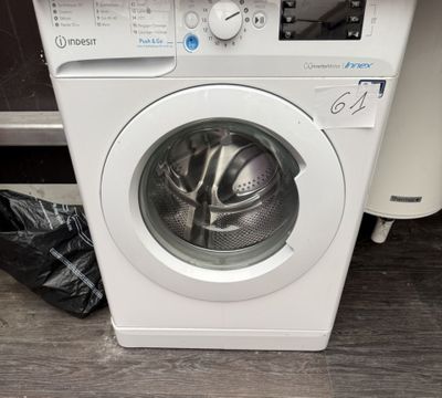 a white washing machine sitting on the floor next to a trash bag