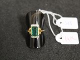 an image of a ring with a green stone on top of a black surface