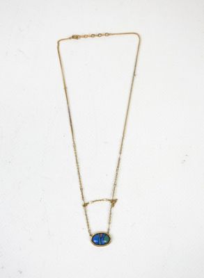 Un collier en or orné d'une pierre oplite bleue est suspendu sur un fond blanc