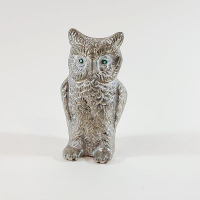 a silver owl figurine with green eyes on a white background