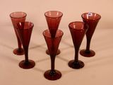 four red wine glasses are lined up on a white surface