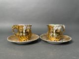 two cups and saucers decorated with gold and white flowers