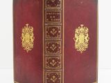 an old red book with gold trim sitting on top of a white table