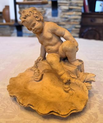 une statue représentant un garçon assis sur un coquillage posé sur une table