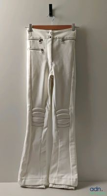 white jeans with zippers hanging on a hanger against a wall